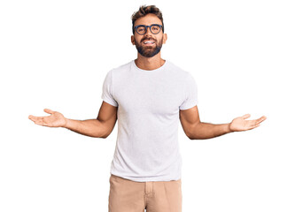 Young hispanic man wearing casual clothes and glasses smiling showing both hands open palms, presenting and advertising comparison and balance