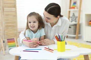 Mother and her little daughter drawing with colorful pencils at home