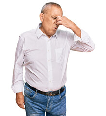 Handsome senior man wearing elegant white shirt smelling something stinky and disgusting,...