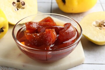 Tasty homemade quince jam in bowl and fruits on tiled table, closeup