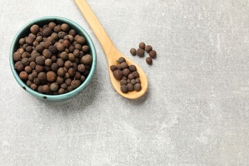 Aromatic allspice pepper grains in bowl and spoon on grey table, top view. Space for text