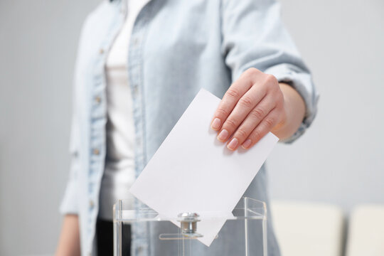 Woman putting her vote into ballot box on blurred background, closeup