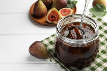 Jar of tasty sweet jam and fresh figs on white wooden table. Space for text
