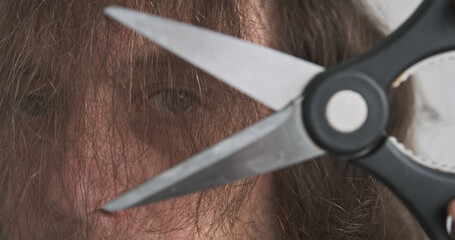Male face covered with hair. Man cuts with scissors against own eyes. Long hair, close-up. Concept for solving an issue, problem, hair interferes vision - obrazy, fototapety, plakaty