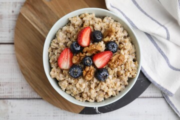 Tasty oatmeal with strawberries, blueberries and walnuts in bowl on white wooden table, top view
