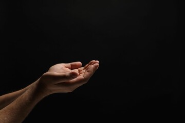 Religion. Man with open palms praying on black background, closeup. Space for text