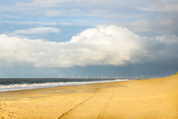 The sunny beach near Ouddorp in the Netherlands with the Maasvlakte and its wind turbines in the distance under a menacing sky with a thunderstorm passing.