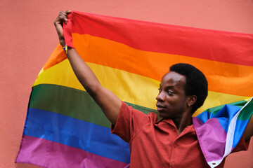 Gay black man holding a rainbow flag representing the diversity and inclusivity of the LGBTQ...