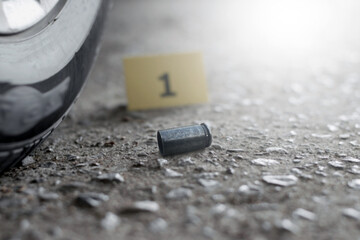 Pistol bullet shell on cement floor in front of number one yellow paper near car wheel, concept for investigation and crime by using gun, soft focus.
