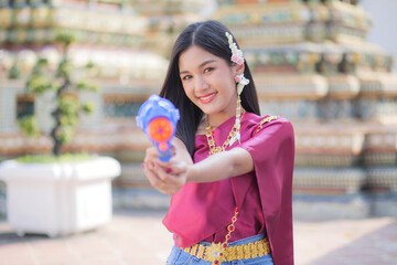 Portrait cheerful young asian woman holding plastic water gun Smiling and having fun playing in the water Songkran festival, Thailand. isolated on pink background. Thai New Year's Day.