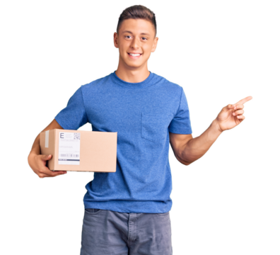 Young handsome hispanic man holding delivery package smiling happy pointing with hand and finger to the side