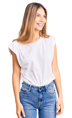 Beautiful caucasian woman with blonde hair wearing casual white tshirt looking away to side with smile on face, natural expression. laughing confident.