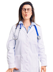 Fototapeta premium Young beautiful woman wearing doctor stethoscope and glasses making fish face with lips, crazy and comical gesture. funny expression.