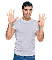 Handsome hispanic man wearing casual white t shirt showing and pointing up with fingers number nine while smiling confident and happy.