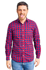 Fototapeta premium Handsome young man with bear wearing casual shirt sticking tongue out happy with funny expression. emotion concept.