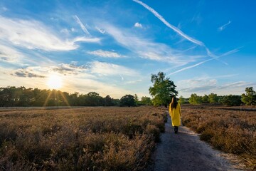 A girl in a yellow coat from behind walking on a countryside path on a sunny day