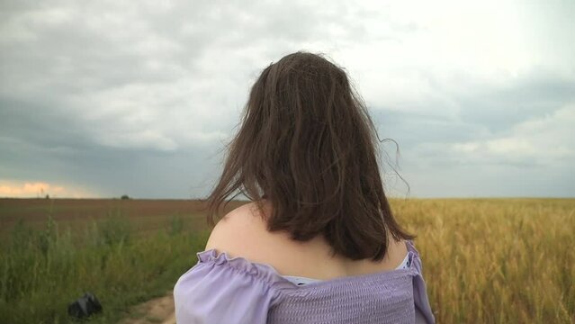 A girl in a dress runs near a field of wheat. Cloudy day. Wavy hair