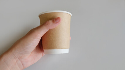 Hand holding a brown disposable paper cup.