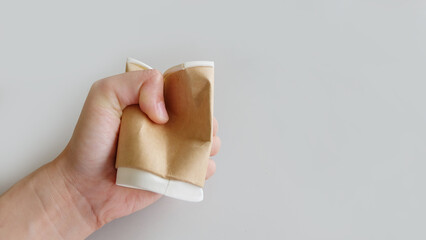 Hand holding and crushing a brown disposable paper cup.