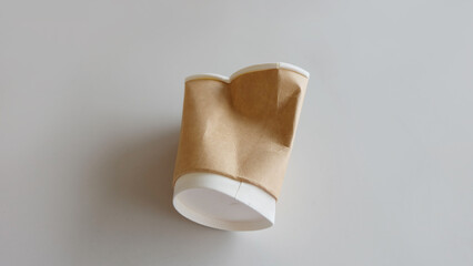 A crumpled brown disposable cup, laying on a gray surface.