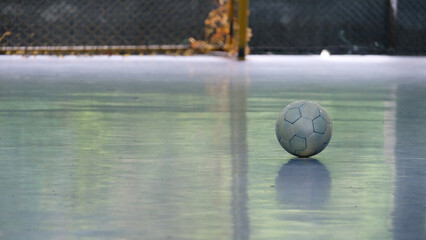 A lone futsal ball, on the ground of an empty futsal court, with the base of the goal net visible...