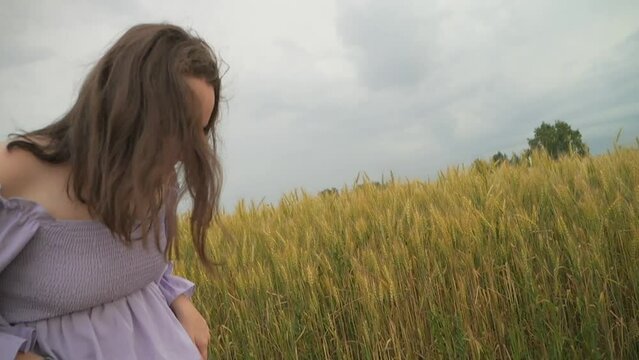A girl in a dress runs near a field of wheat. Cloudy day. Wavy hair
