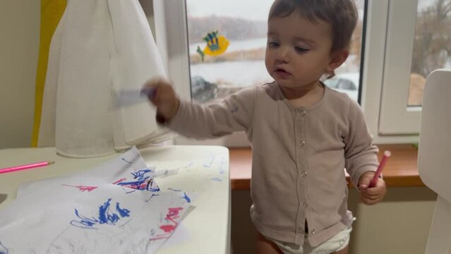 child draws with pencils on a sheet. happy family child dream concept drawing. baby girl lies on the floor indoors and draws pictures , developing fine motor skills. lifestyle child of a