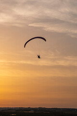 A paraglider or paramotor flying during a beautiful sunset over the beach. Real Photo