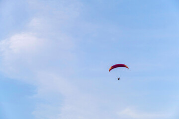 A paraglider or paramotor flying over a beautiful blue sky with white clouds over the beach.Real Photo
