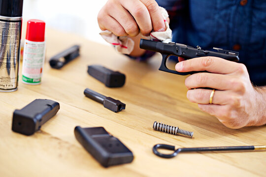 Hands, man with gun cleaning process at table for safety, self defense and handgun assembly. Caution, equipment and person with firearm maintenance with cloth, magazine and wiping dust, dirt and oil