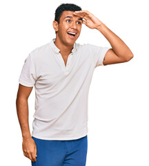 Fototapeta premium Young arab man wearing casual clothes very happy and smiling looking far away with hand over head. searching concept.