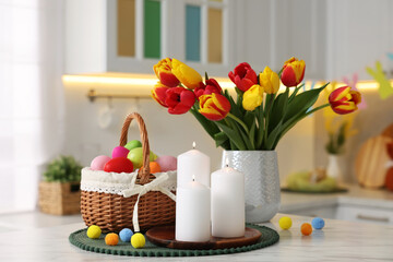 Easter decorations. Bouquet of tulips, painted eggs and burning candles on table indoors, closeup