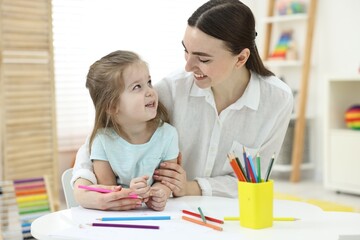 Mother and her little daughter drawing with colorful pencils at home