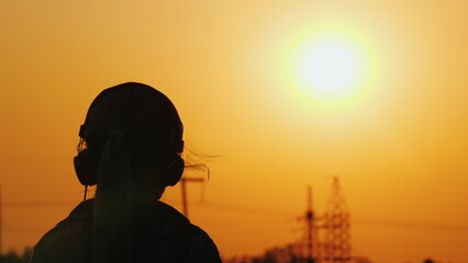 Girl in headphones listening to the radio on the background of the cityscape and beautiful orange sky at sunset