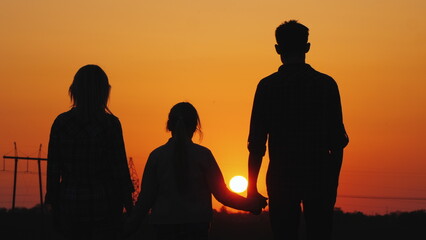 Family of three admiring the orange sunset over the city, rear view