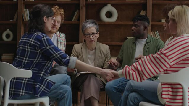 Therapy group participants engage in a supportive handholding activity, facilitated by a therapist, to build trust and connection