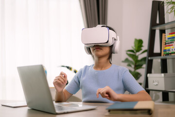 A woman wearing a virtual reality headset is sitting at a desk with a laptop