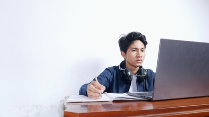 young Asian male student is studying in front of a laptop, doing assignments
