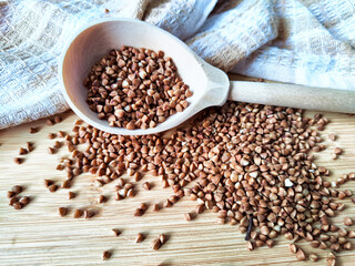 Buckwheat scattered on textured fabric and in a wooden spoon. Grits for cooking. Texture, background, copy space and place for text