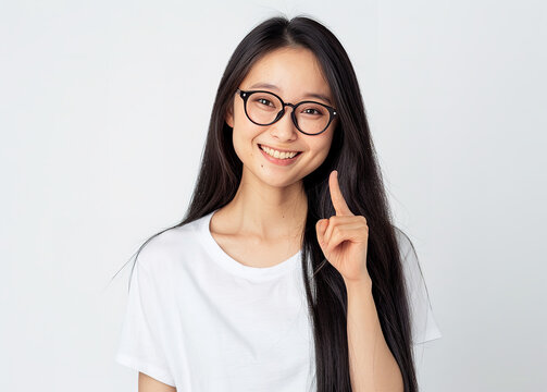 A realistic photo of an Japanese artist with long straight black hair, wearing glasses and a white t-shirt pointing at something on the side with her right hand, with a smiling facial expression