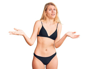 Young beautiful blonde woman wearing bikini clueless and confused with open arms, no idea concept.