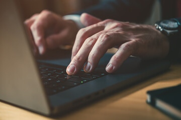 Closeup of male hands typing laptop computer keyboard at office desk, businessman working late at...