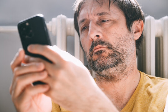 Man using cellphone at home while leaning on the heating radiator
