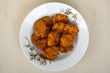 Crispy fried lentils with onion called Piyaju or Daler Bora on a white plate on a wooden background. Top view of spicy onion fritters which is a very popular snack in Bangladesh.