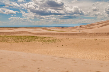 An expansive shot of a single figure contrasting against the magnitude of rolling dunes and a wide sky, depicting solitude