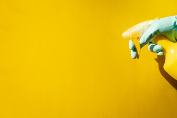 house cleaning concept. hands in blue rubber household gloves hold spray bottle on yellow background.
