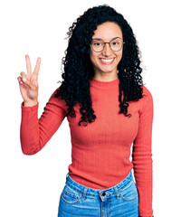 Young hispanic woman with curly hair wearing glasses showing and pointing up with fingers number two while smiling confident and happy.