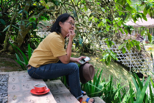 Middle-aged Asian woman sitting alone on the garden patio, enjoying the fresh tropical air