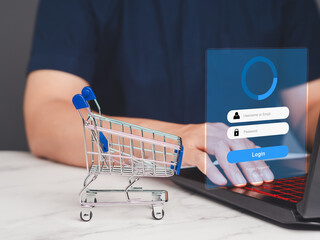 Man is using a laptop with a login screen and a small shopping trolley on a table.