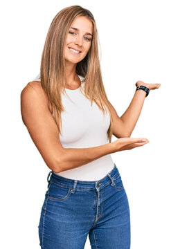 Young blonde woman wearing casual style with sleeveless shirt inviting to enter smiling natural with open hand